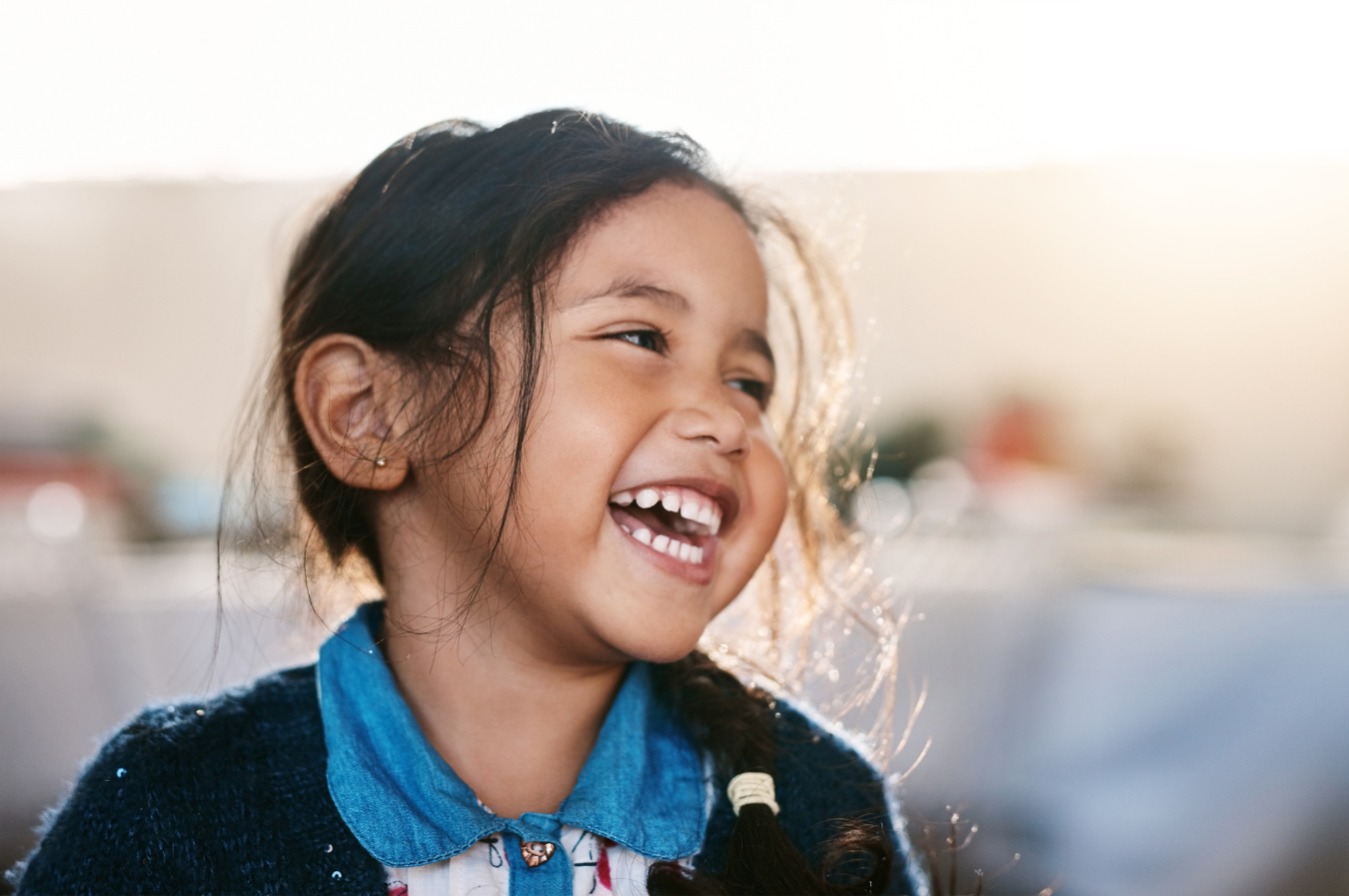 Smiling young girl with long hair, wearing a blue shirt, representing joy and healthy dental health in pediatric dentistry context.
