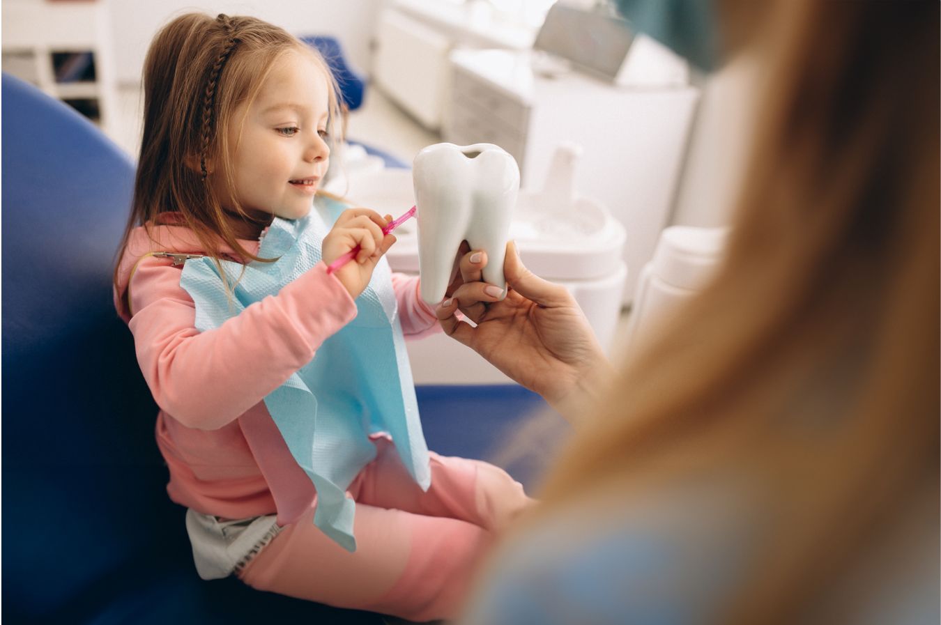 Child smiling and brushing a large dental model during a pediatric dental visit, emphasizing the importance of dental hygiene and education for kids.
